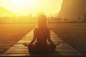 Mujer sentada en posición de meditación, de frente a amanecer